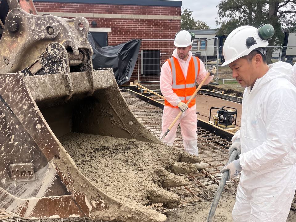 Excavator bucket discharging concrete onto mesh