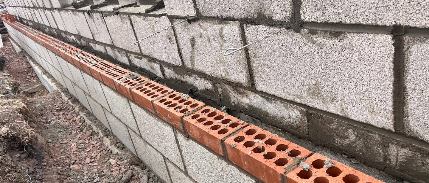 Block wall with a course of perforated bricks and wall ties
