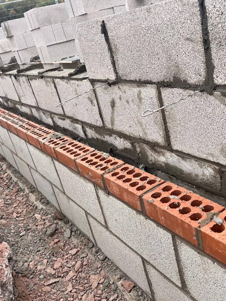 Block wall with a course of perforated bricks and wall ties