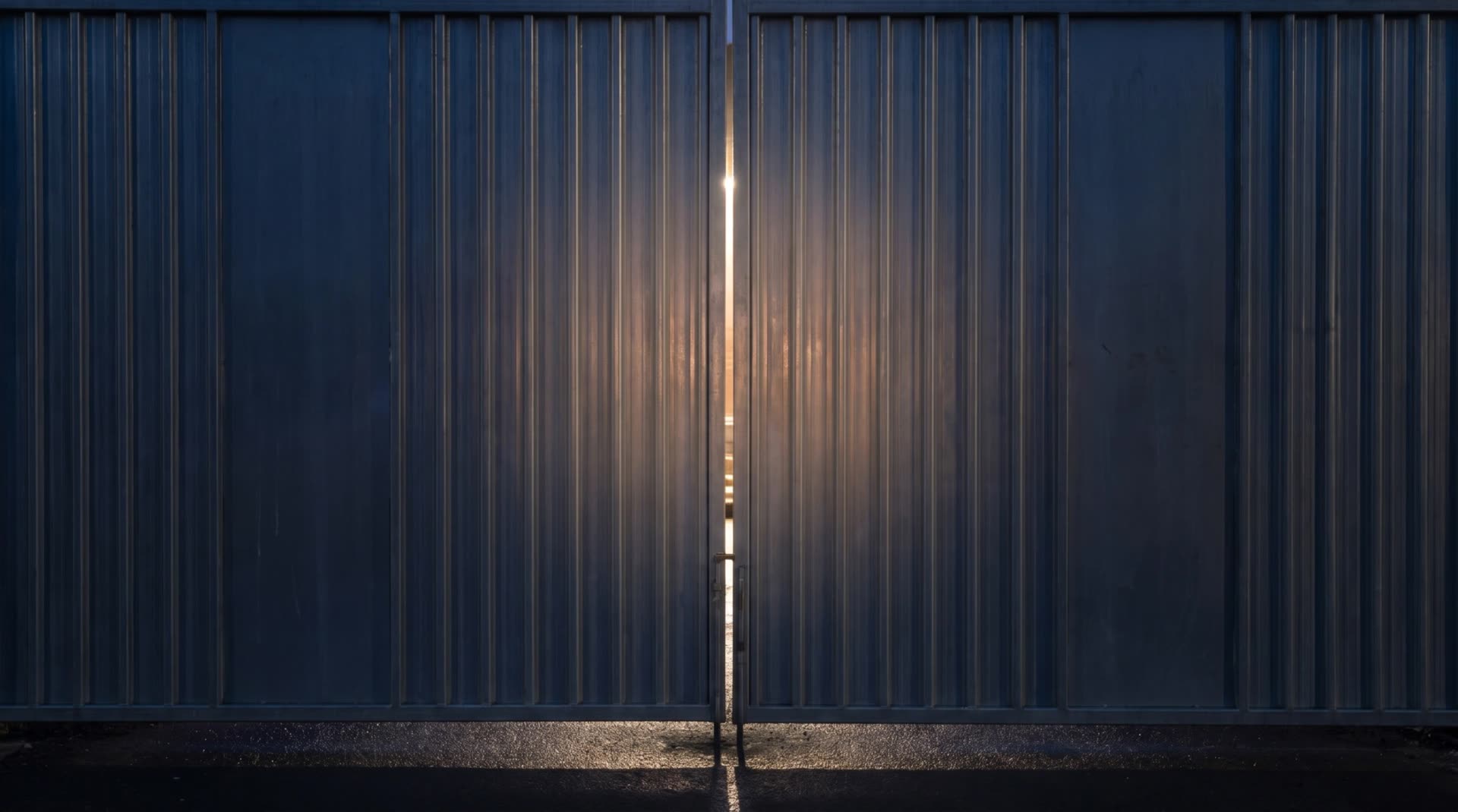 Closed steel site gates at night, floodlight glow through the gap